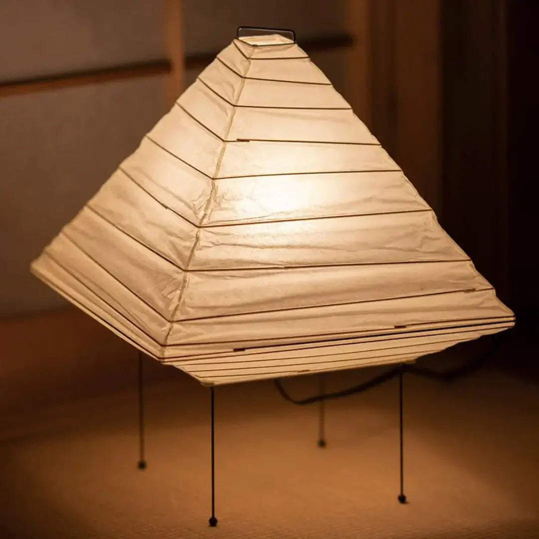 Handcrafted washi paper shade encasing a metal frame, casting warm amber gradients on a minimalist wall like ink-wash paintings at dusk.