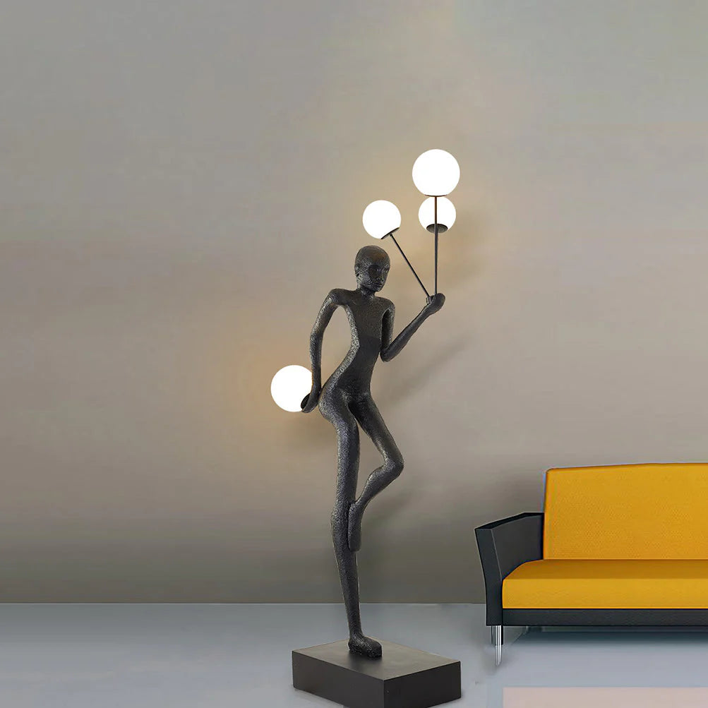 The black Amelia Sculpture Floor Lamp stands out next to the orange and black sofa, and its spherical bulb emits soft white light.