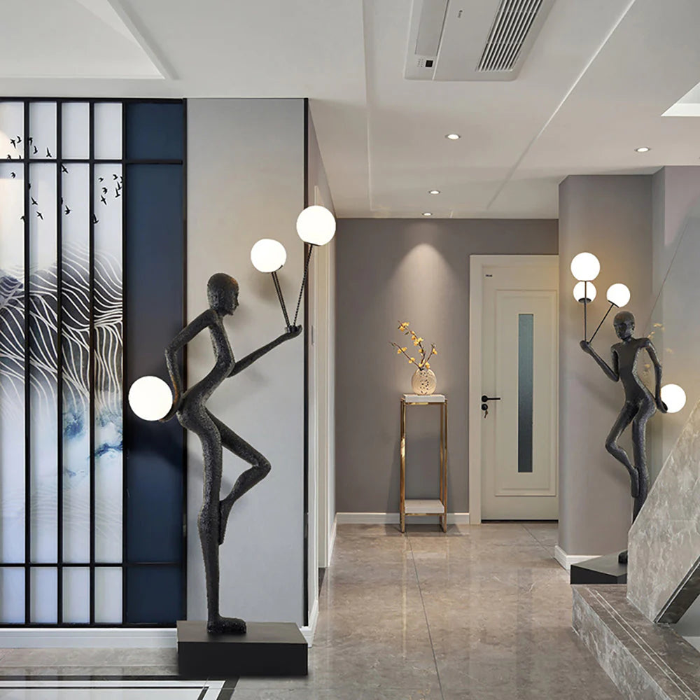In the entrance corridor, two black human-shaped floor lamps stand on both sides, with soft spherical lights. The blue and white screen, gray wall and golden side table complement each other.