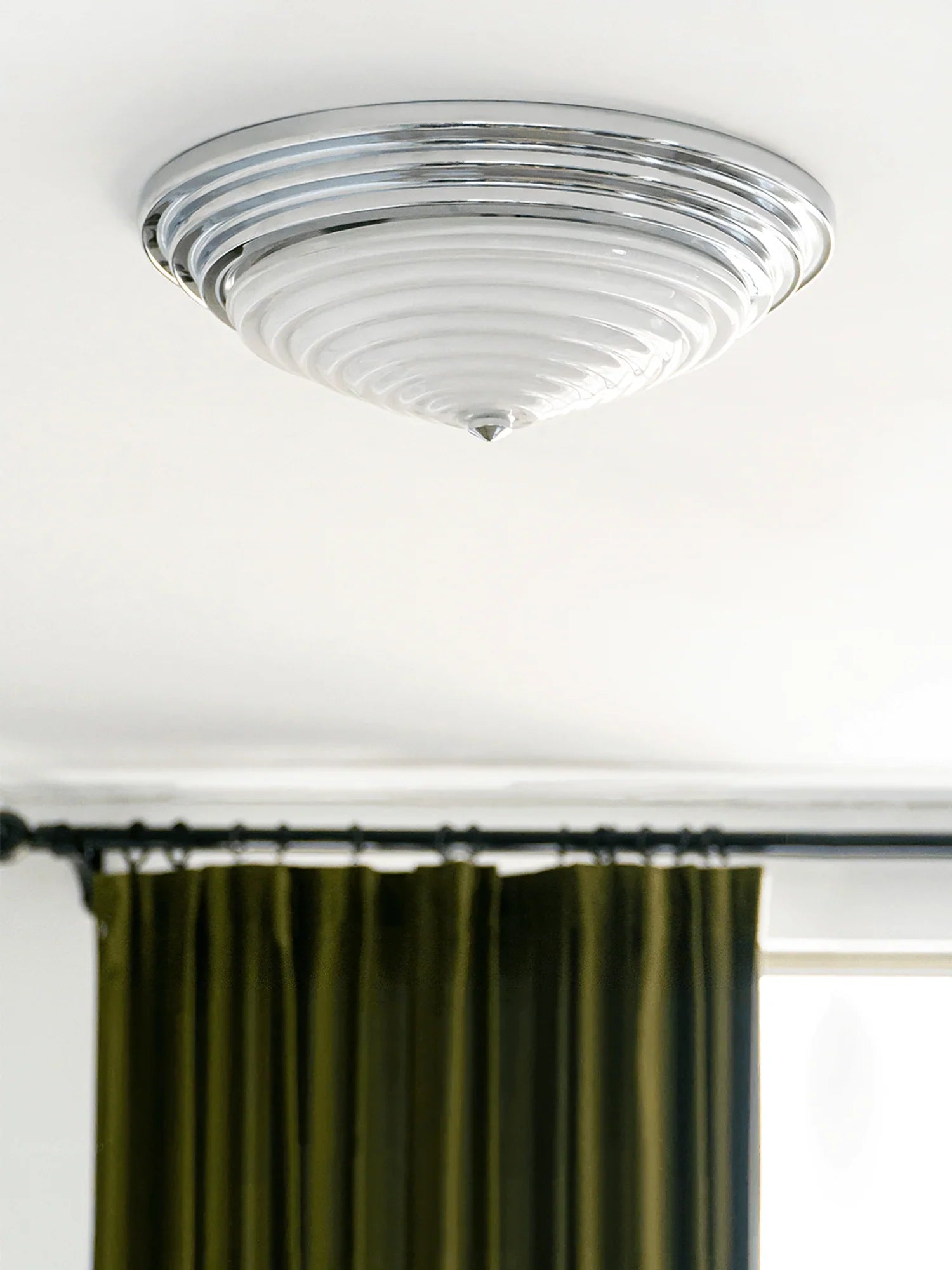 The American Circle Ceiling Light with a chrome body is hung on the ceiling next to the curtains.