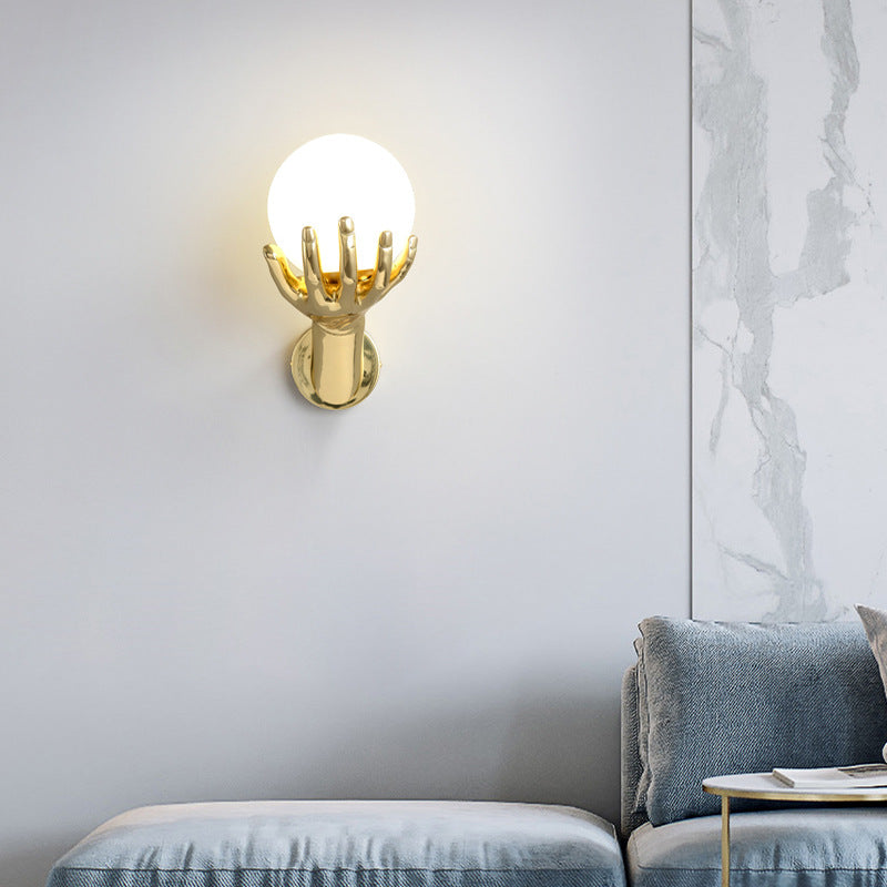 In the simple space, the golden hand-shaped wall lamp emits soft light, illuminating the light gray wall, and next to it is a sofa with gray pillows and an exquisite side table.