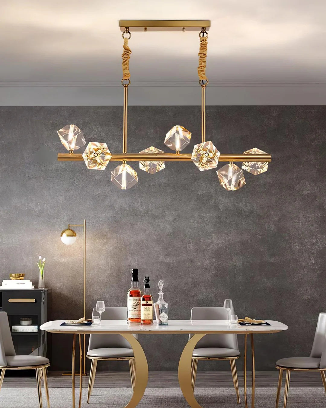 In a modern - styled dining space, a Polyhedron Crystal Chandelier with a golden frame and sparkling crystal elements gracefully hangs from the ceiling. It illuminates the dining table below, which is adorned with elegant tableware and bottles, creating a sophisticated and inviting atmosphere.