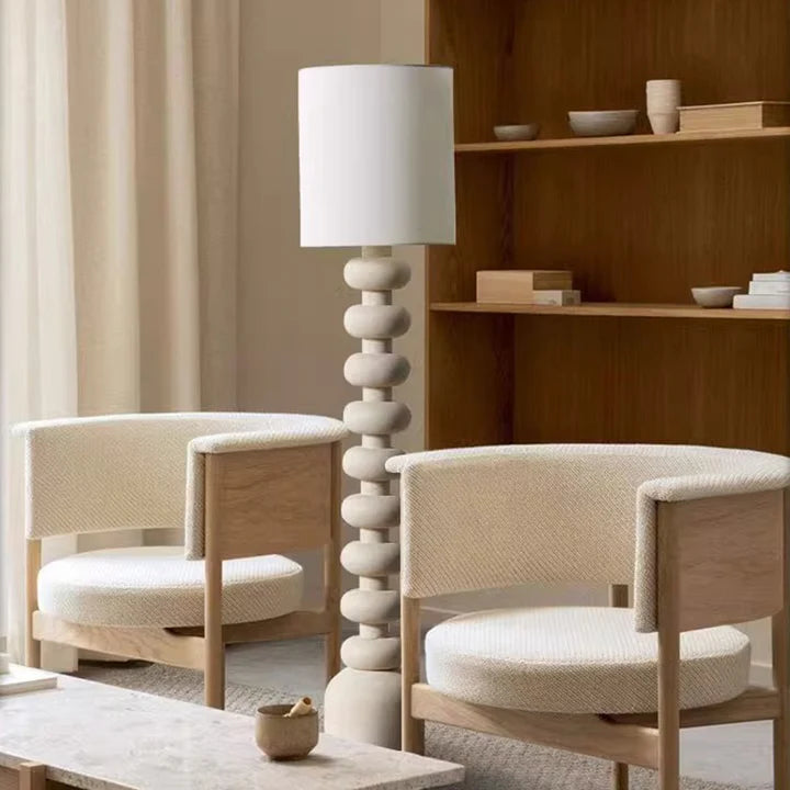 The lamp’s resin structure (rounded layers) pairs with a fabric shade, releasing light that fits the room’s minimalist warmth.