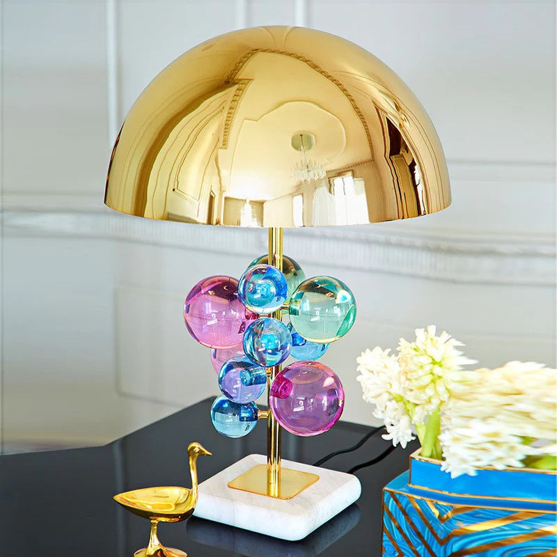 A lamp featuring a shiny golden dome shade, colorful glass spheres, and a marble base, ideal for modern setups.