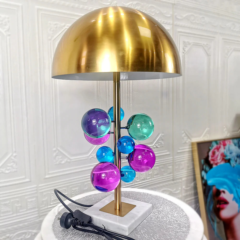 Polished golden hood pairs with pastel glass globes and a marble base, adding charm to study areas.