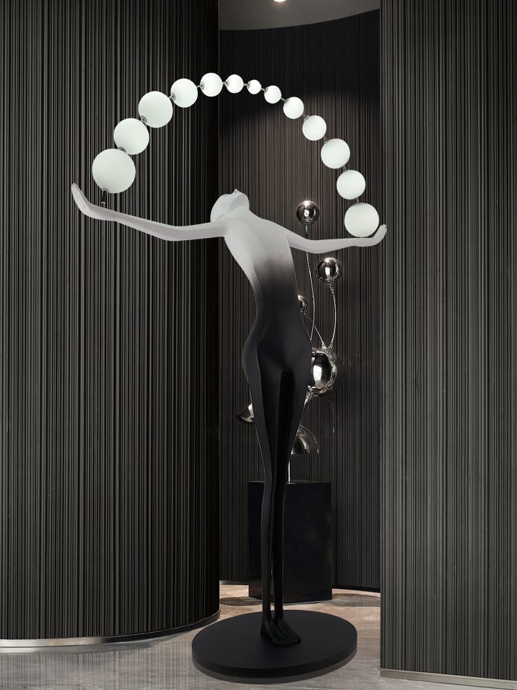 The human-shaped floor lamp is placed in front of the artistic black wall, adding the finishing touch.