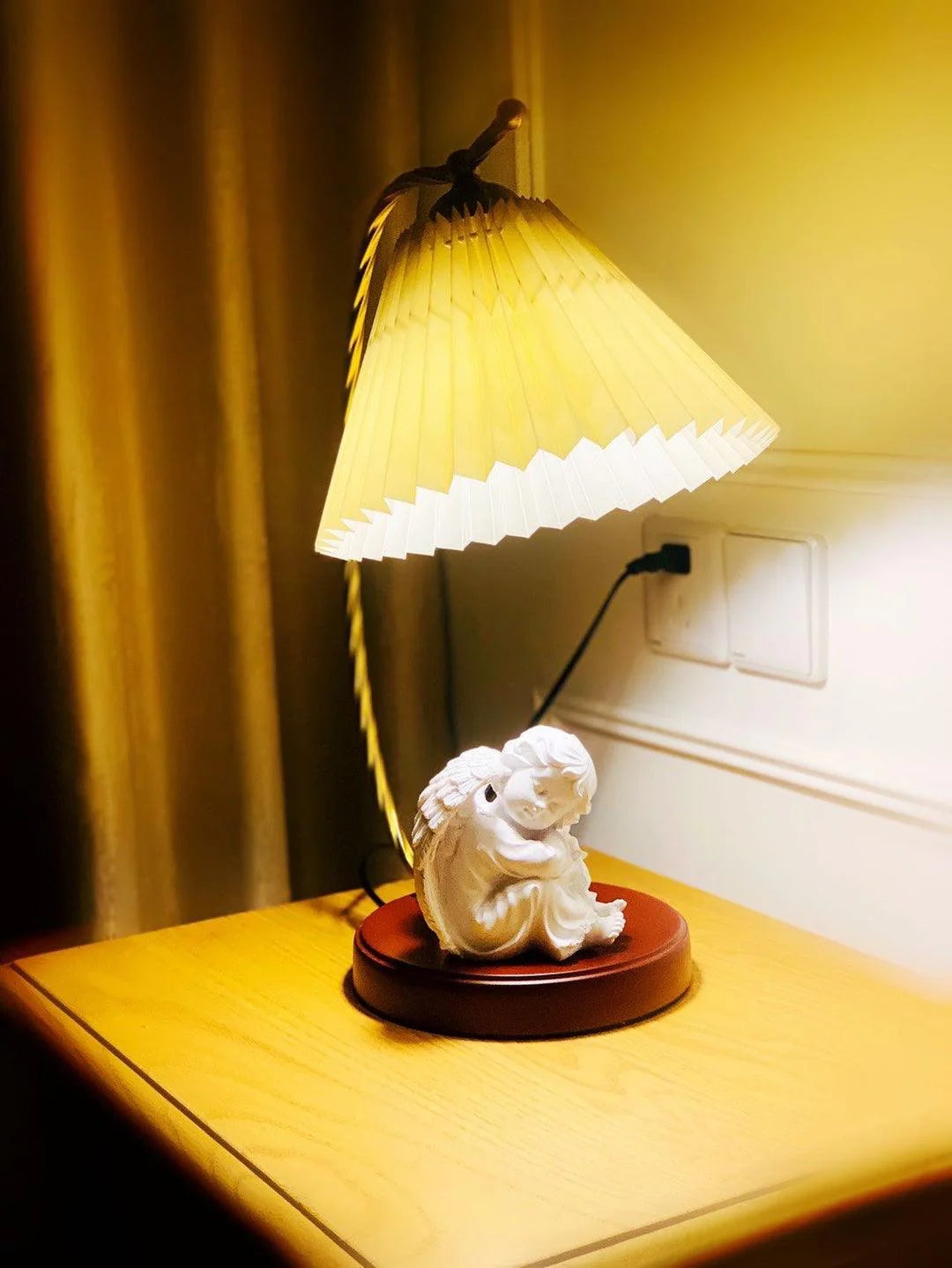 The French pleated table lamp emits a warm glow on the bedside table, with a peacefully sleeping little angel resting on its base.