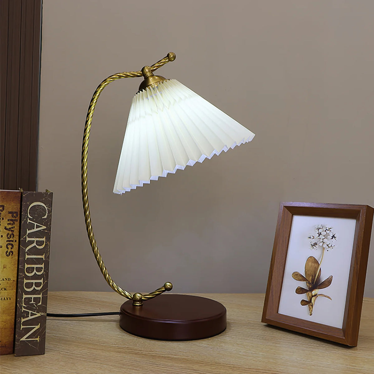 This table lamp features a white pleated lampshade, a wooden base, and a vine-like copper-toned metal piece that elegantly connects the two parts.