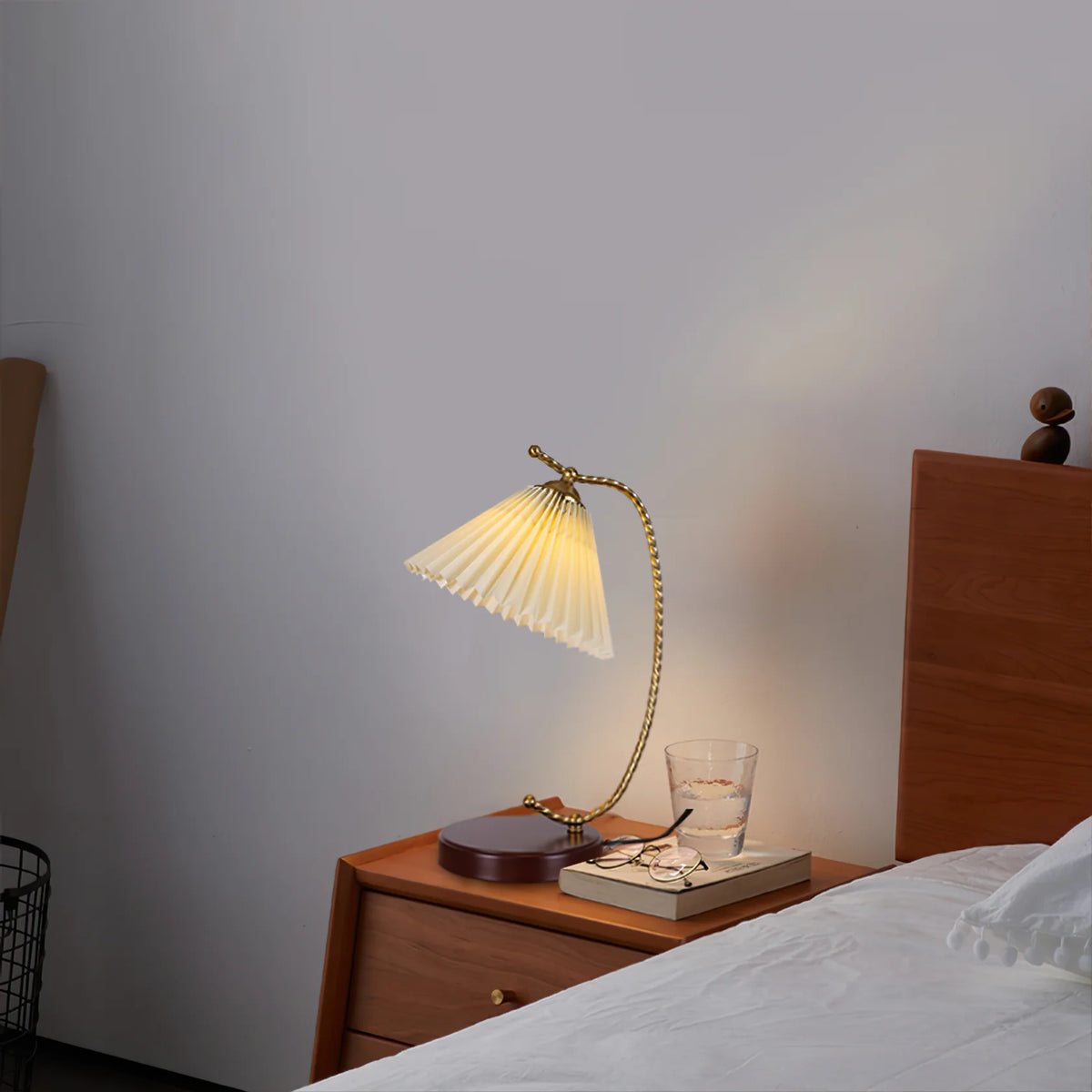 The French fabric table lamp glows softly on the bedside table, accompanied by a few books and a pair of glasses.