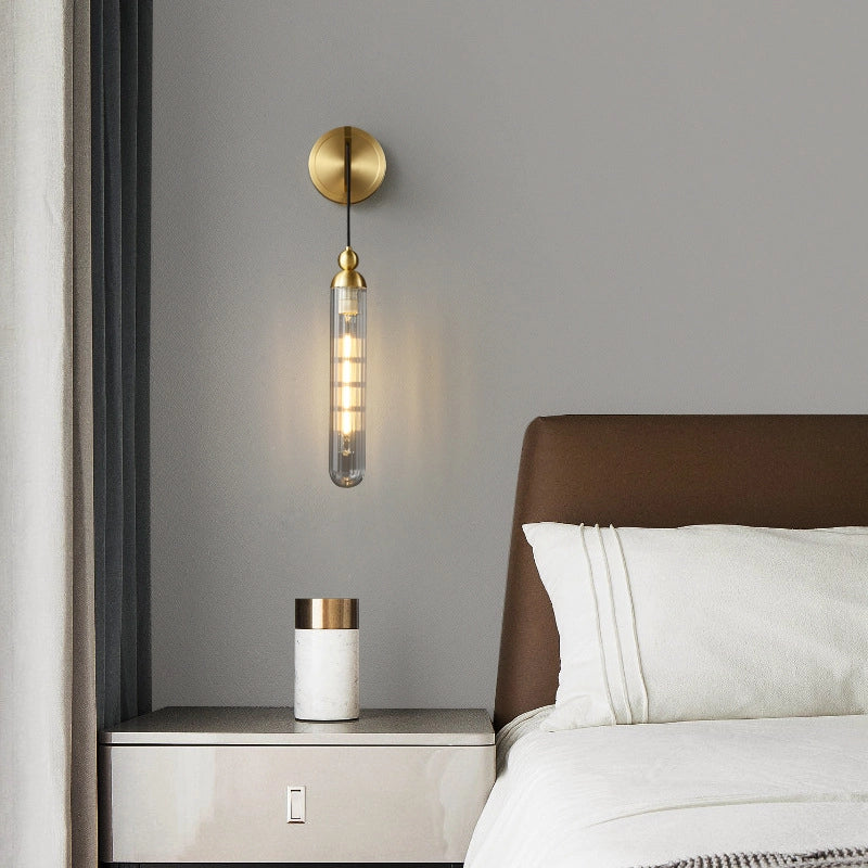 On the light gray wall_a simple wall lamp emits soft warm light_and the golden round base and transparent lamp tube are set off_which is exquisite and elegant.