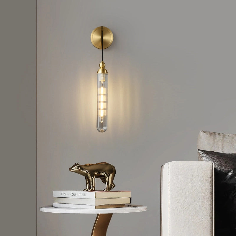 The simple style wall lamp hangs on the gray wall_with a golden round base and a transparent lamp tube_and the warm light is soft.On the small whiteround table below_a golden bear ornament is place do