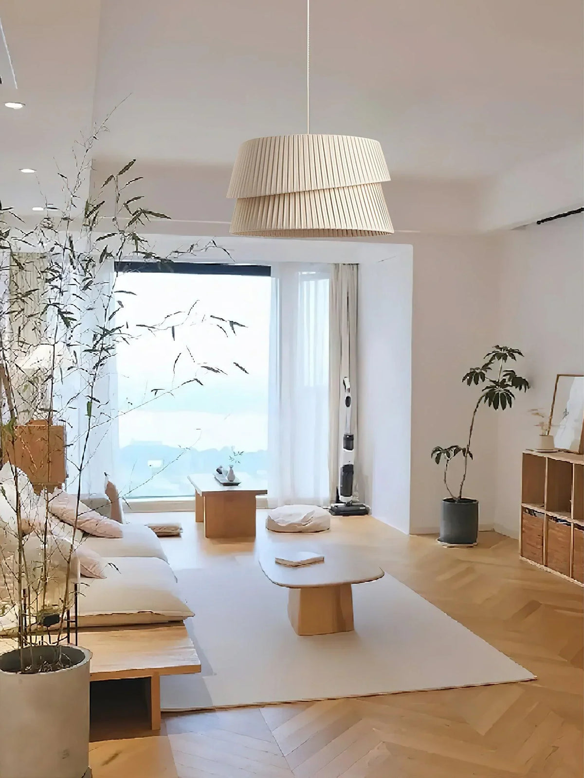 In the spacious and bright living room, a pleated texture chandelier made of fabric hangs in the air. Large windows bring in plenty of natural light, and the wooden floor is matched with light-colored soft furnishings.