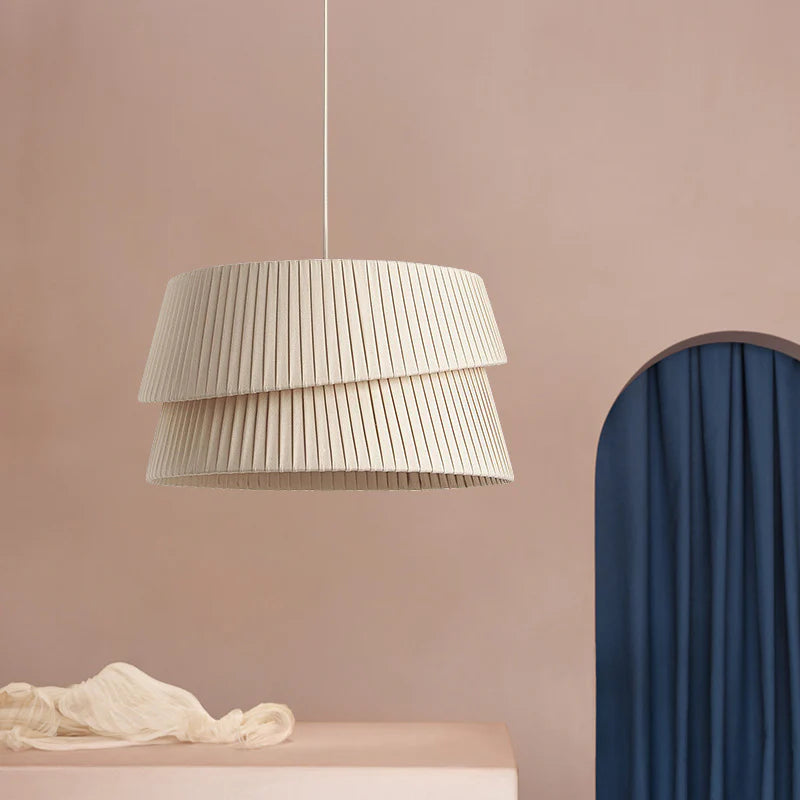 A Westwing Nyla Pendant Light hangs elegantly in front of a light pink background. Its simple shape exudes a soft beauty.