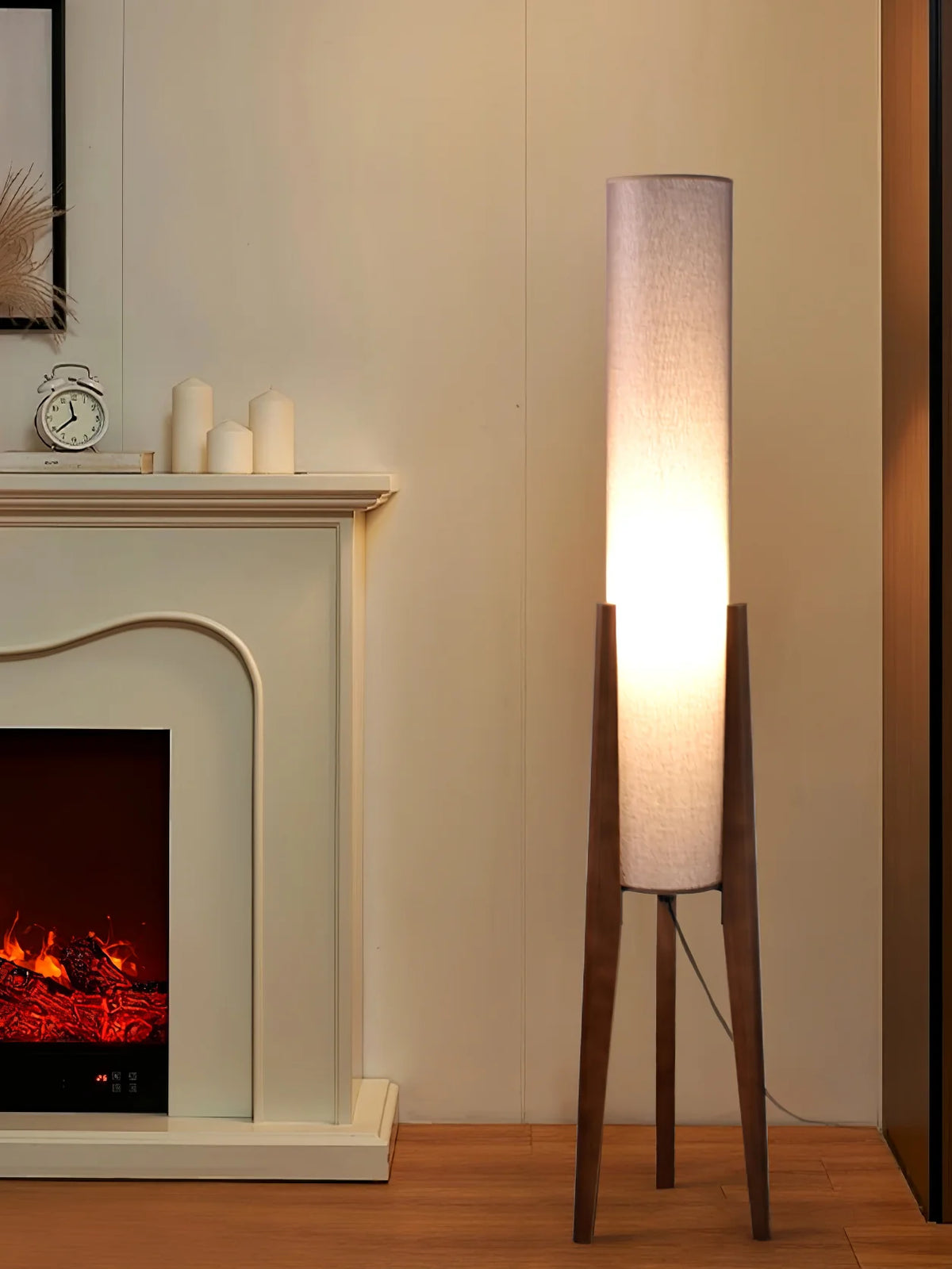 Next to the fireplace, the original wood tripod floor lamp is lit with soft white light.