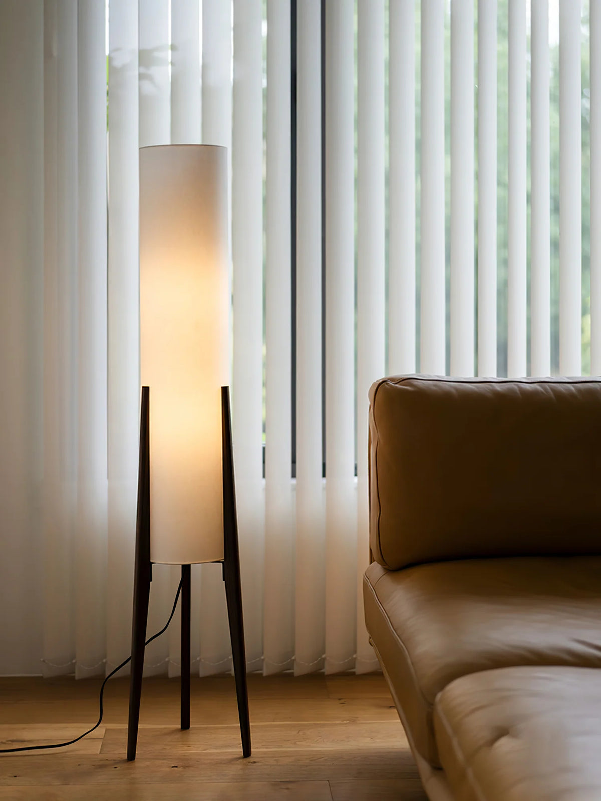 By the window, the Japanese Zen floor lamp emits soft warm light, matched with a light brown sofa and white curtains, creating a comfortable and quiet home atmosphere.