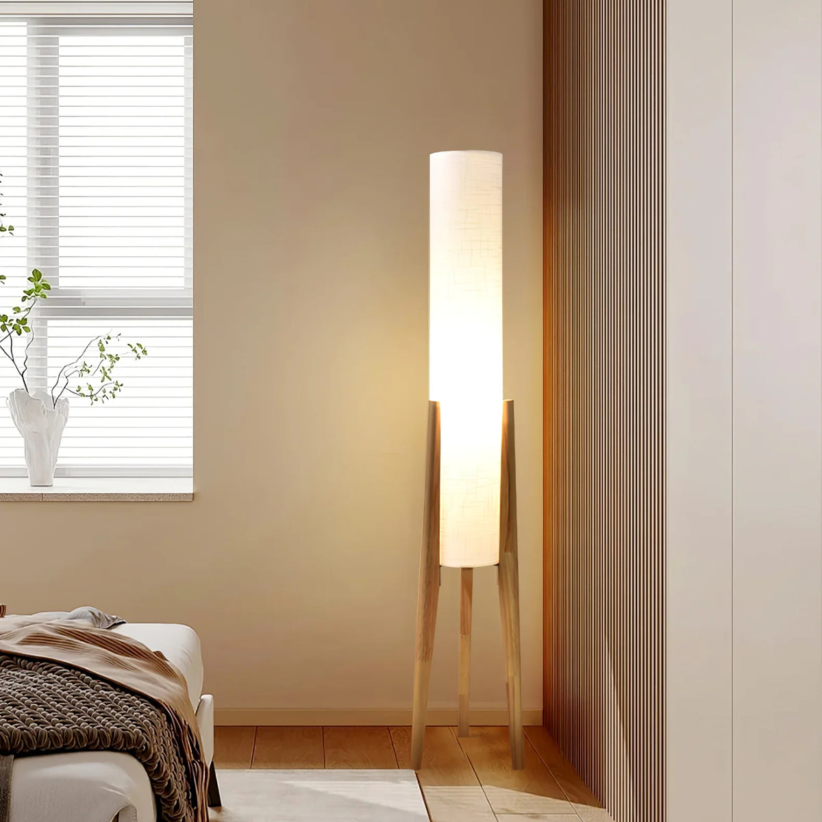 The Zen floor lamp supported by three wooden legs emits soft light beside the bed.