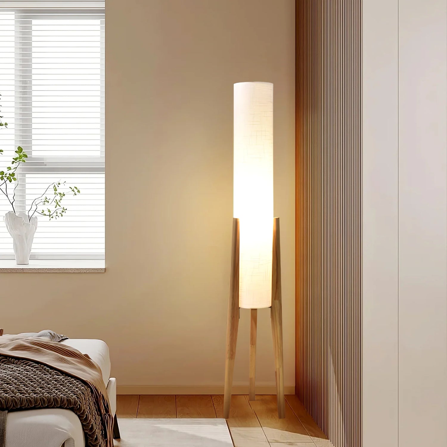 The Zen floor lamp supported by three wooden legs emits soft light beside the bed.