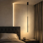 Matte black linear cylinder pendant light illuminated beside cozy bedroom headboard