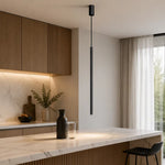 Slim black tube pendant light glowing over marble kitchen island counter with stool