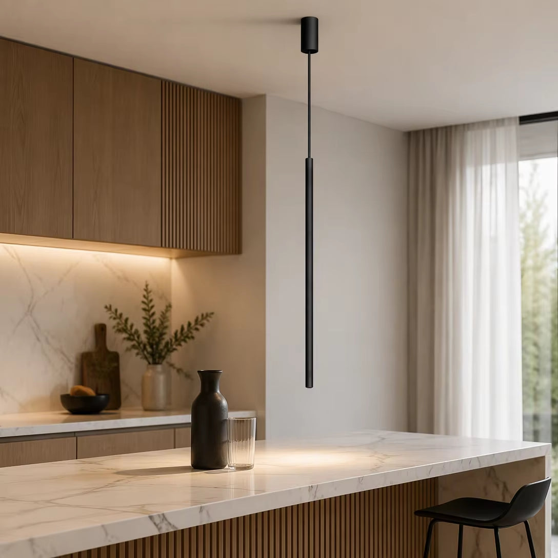 Slim black tube pendant light glowing over marble kitchen island counter with stool