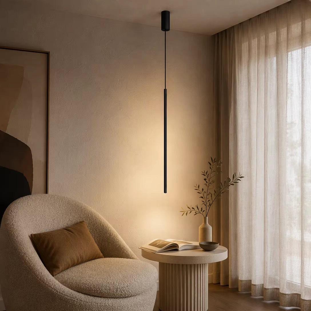Modern black cylinder hanging light casting warm light over cream boucle armchair