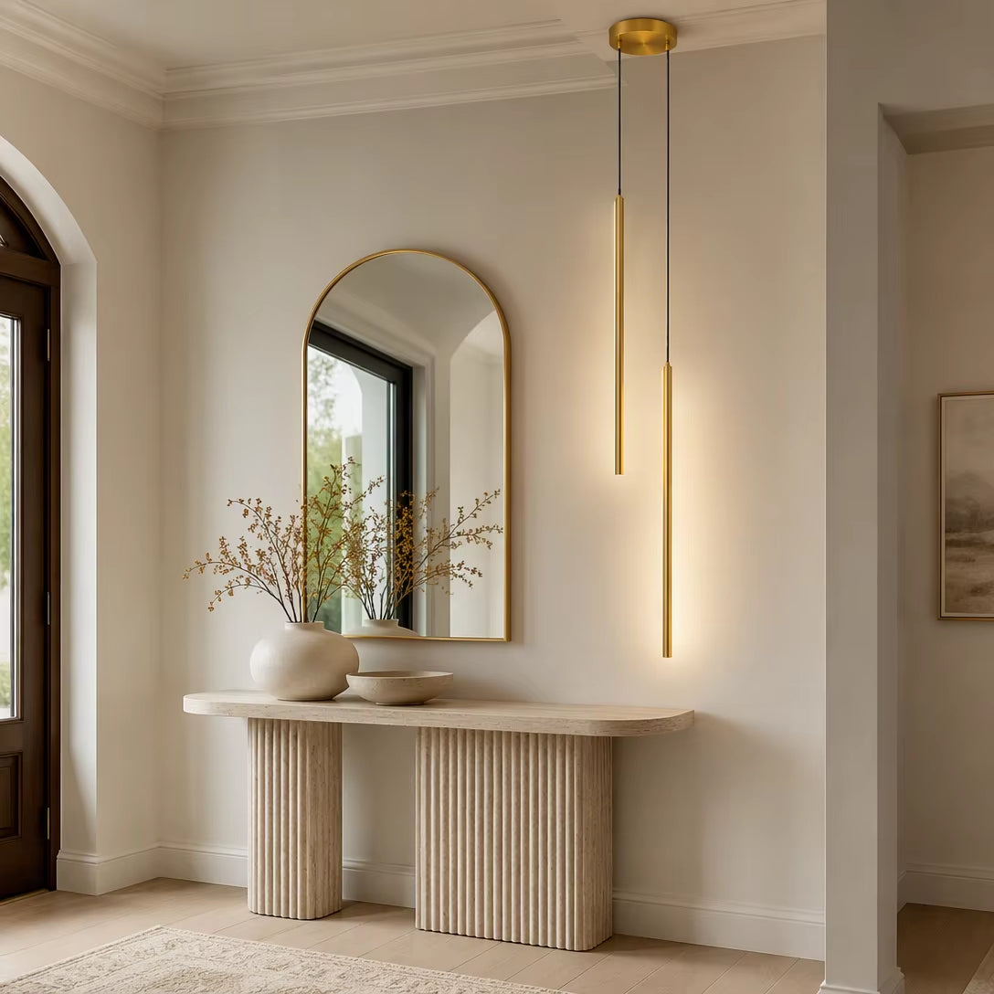 Pair of brushed brass cylinder pendant lights glowing above fluted console table