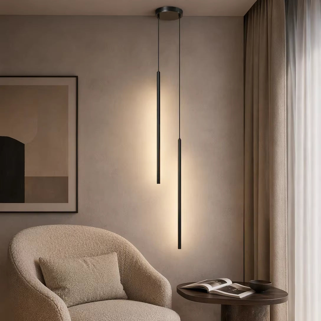 Two light matte black cylinder pendant lamps hanging staggered near lounge chair