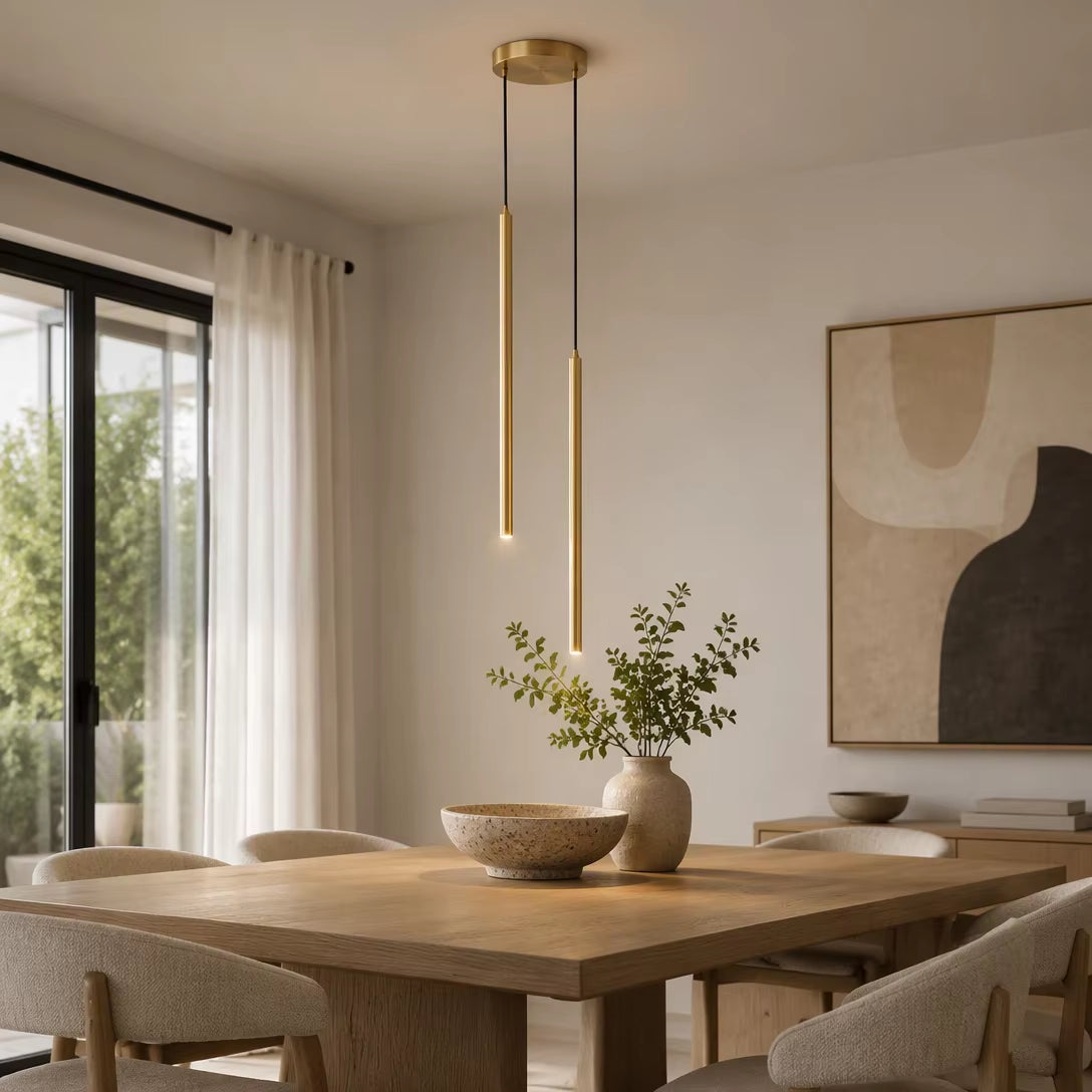 Staggered gold cylinder pendant lights illuminated above natural wood dining table