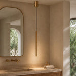 Brushed brass cylinder pendant light illuminated above travertine bathroom vanity