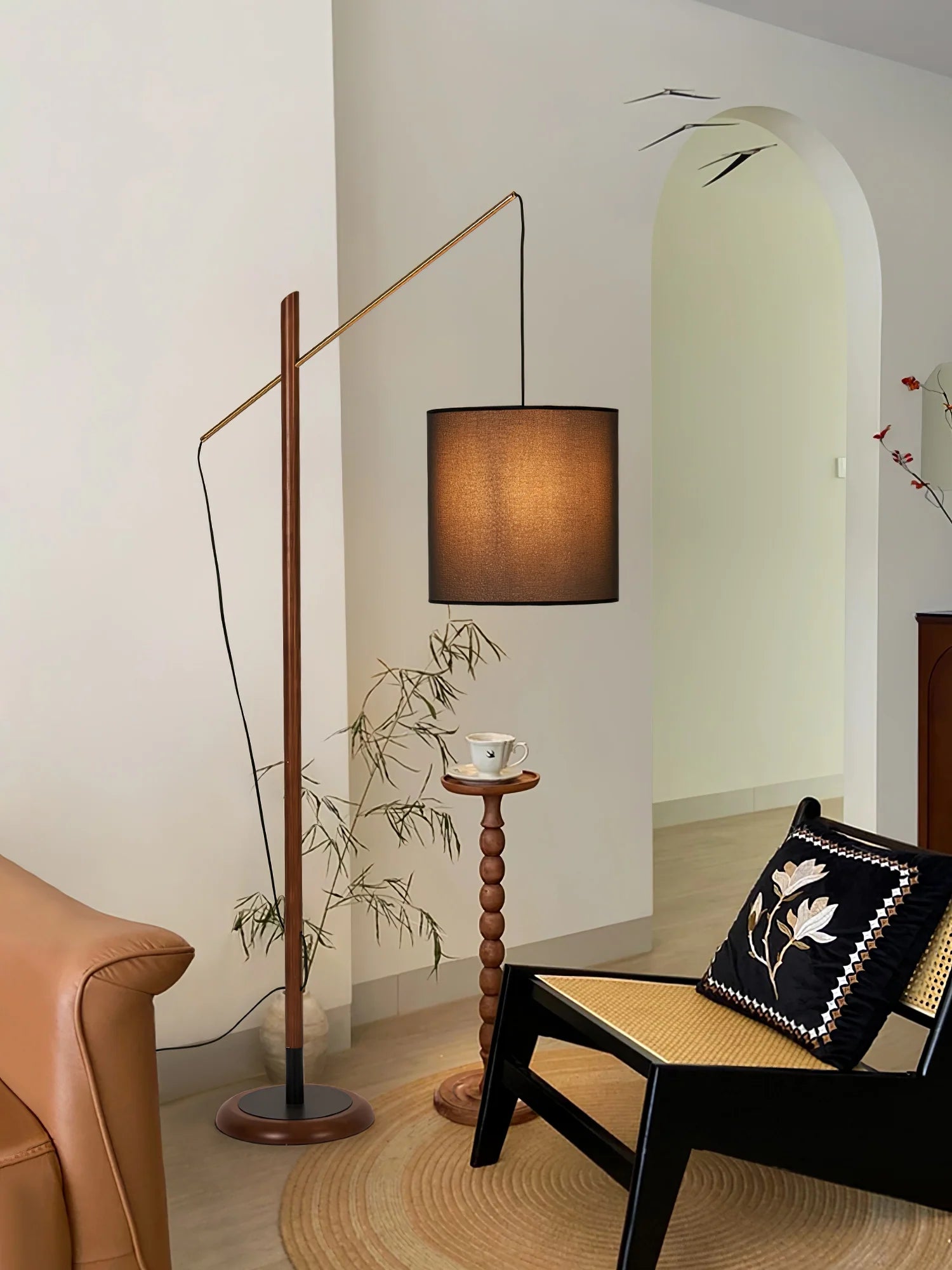 Lit Archer Floor Lamp with dark wood pole stands beside rattan chair and bamboo decor in cozy room