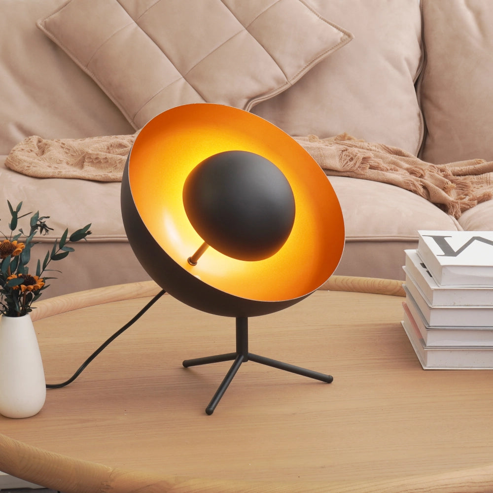 The black mid-century tripod table lamp sits elegantly on a showroom table, adding a touch of classic design to the space.