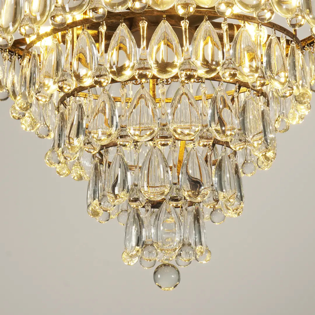 Close‑up view of grape crystal chandelier, glowing teardrop crystal pendants and vintage carved metal trim under warm‑toned light