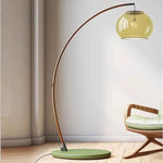 Contemporary Arc Floor Lamp with Glass Shade beside wooden lounge chair, curved wood frame for minimalist living room ambient lighting