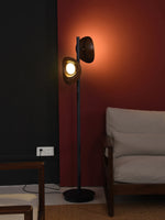 The double-headed wooden floor lamp casts light and shadow on the red wall