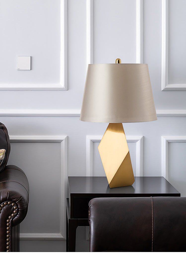 A table lamp with a sleek gold metal surface is placed on the round table next to the sofa