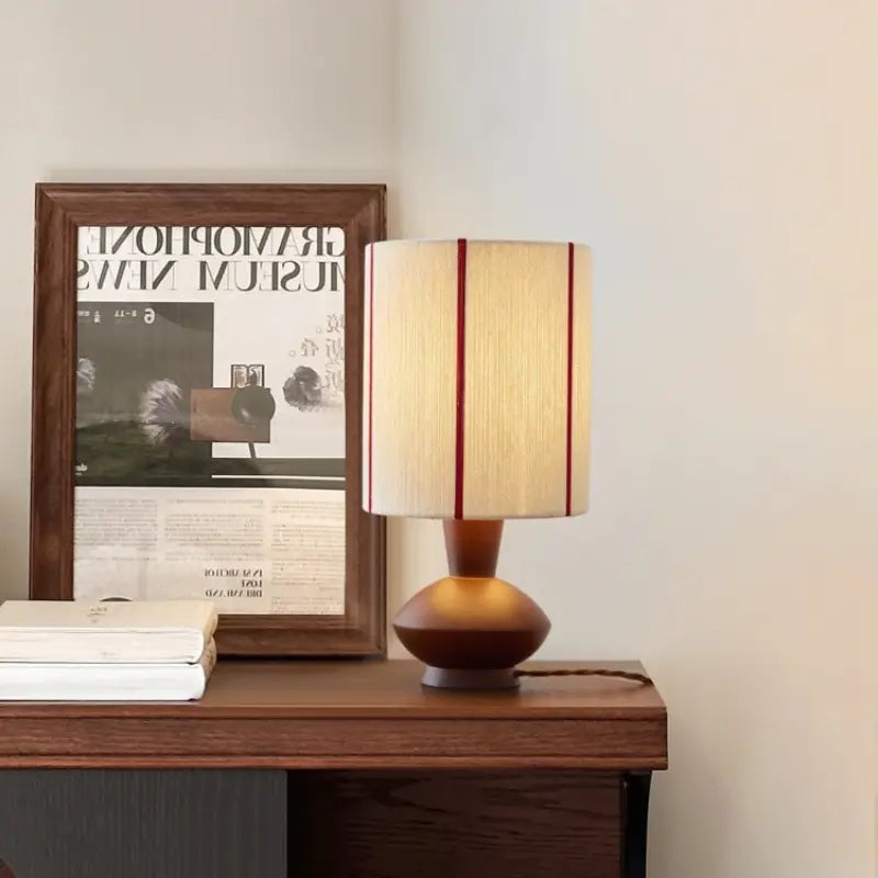 Lit Sora Cotton Woven Table Lamp casts warm glow on wall, sits on nightstand beside plant and books