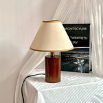 A dark brown wooden Japanese style table lamp is placed on a small round table next to a white curtain