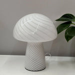Mushroom-shaped table lamp on a white surface with a plant in the background