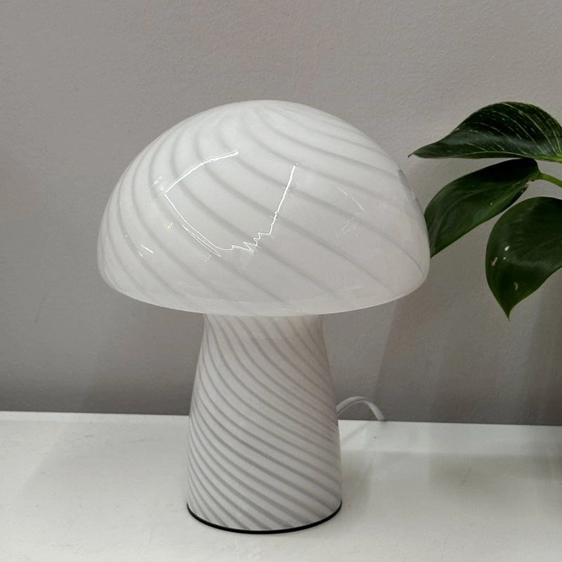 Mushroom-shaped table lamp on a white surface with a plant in the background