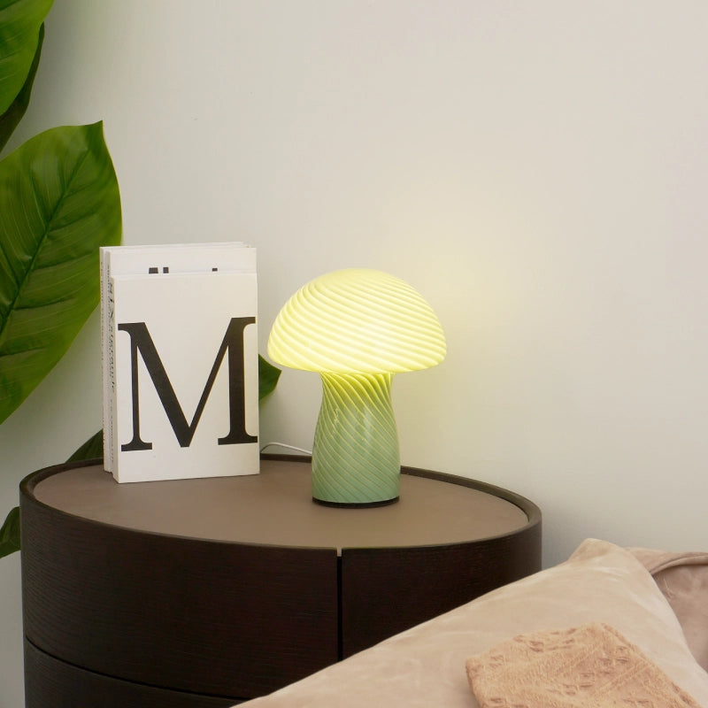 Table lamp on a bedside table with a book and plant in the background
