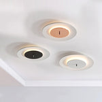 Three simple round ceiling lamps, white outer ring, brown, black and gray in the center, with soft warm light on the edges, decorate the white ceiling.