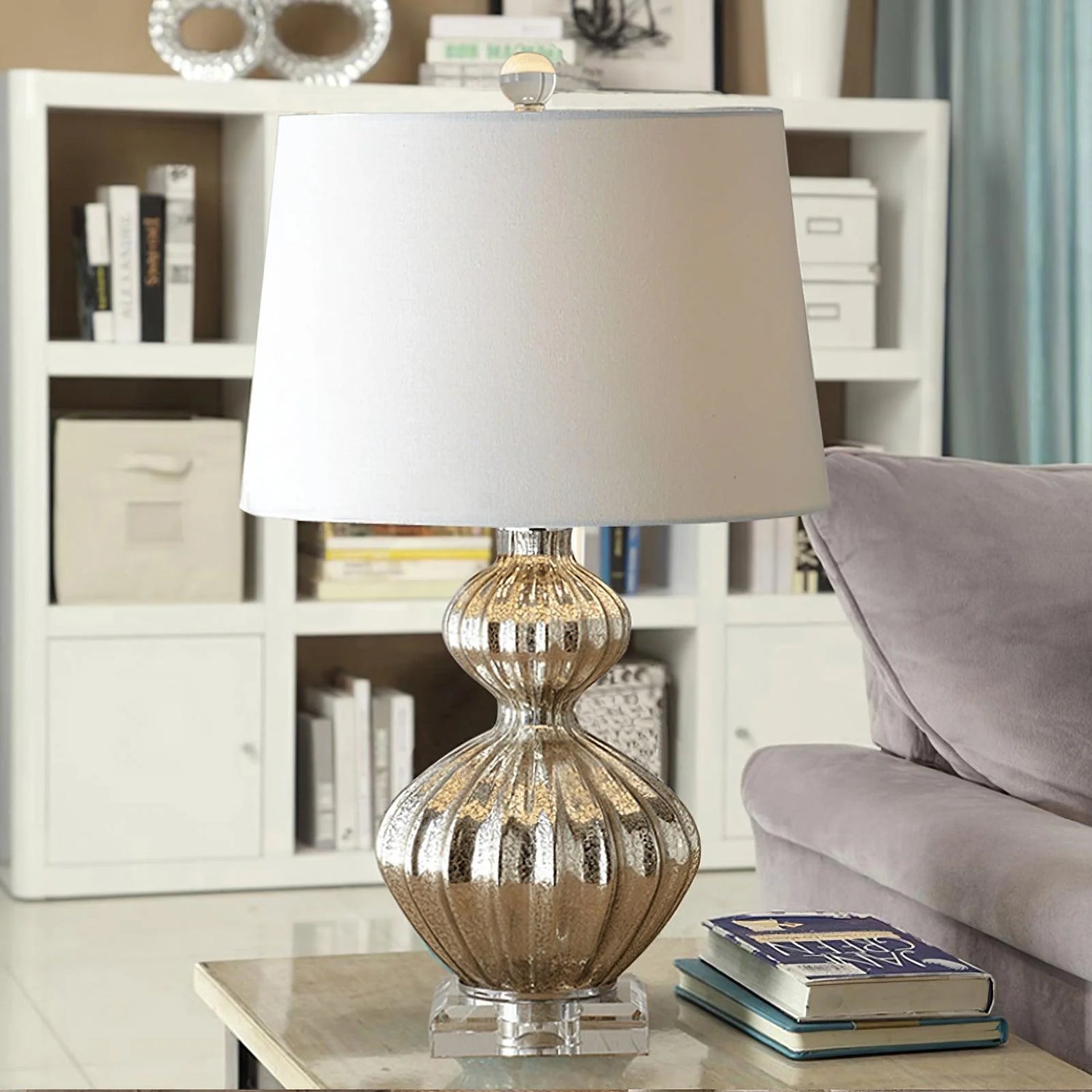 Regency Lili 25 Table Lamp, ribbed mercury glass table fixture placed on marble side table next to fabric sofa and open bookcase