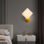 Marble cube wall light emits soft glow, complemented by a shiny golden base for stylish decor.