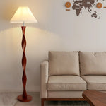 This is a simple and warm living room scene. The main body is a spiral wooden column floor lamp, and the light beige sofa next to it has simple lines. The white wall above is hung with a wooden world map and clock decoration. The marble floor has a natural texture. The overall style is simple and comfortable, and the floor lamp becomes a unique artistic embellishment in the space.