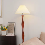 This is a simple and elegant indoor corner with a white wall as the base. The spiral-shaped brown wood floor lamp is matched with a white pleated lampshade, emitting a soft halo.