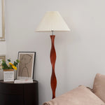 The spiral-shaped wooden floor lamp, paired with a white pleated lampshade, exudes a soft atmosphere. On the black side table next to it, there are paper boxes with yellow flowers, decorative paintings and books.