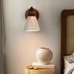Travertine Wabi-sabi Wall Lamp: Wood-base wall light with textured travertine shade, casting soft warm glow in a cozy bedroom (wabi-sabi style).