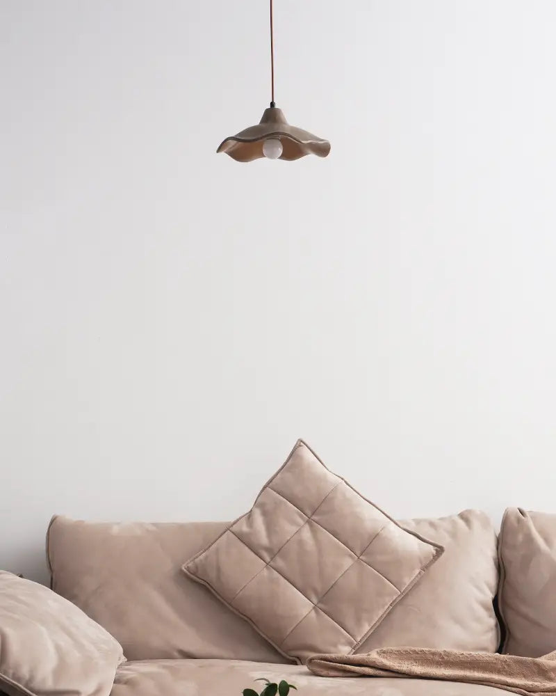 Wavy Cement Pendant Light hanging above a cozy beige couch with a decorative pillow.