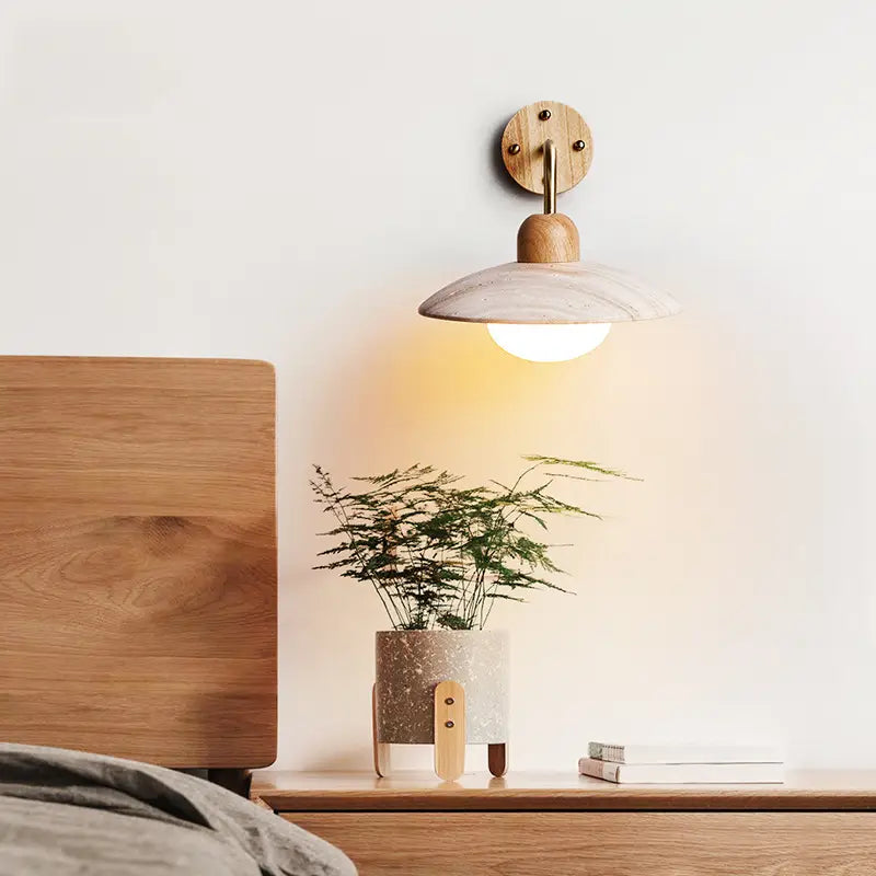 Zanara Travertine Wall Lamp illuminating a bedside table with a plant, showcasing a blend of wood and travertine material.
